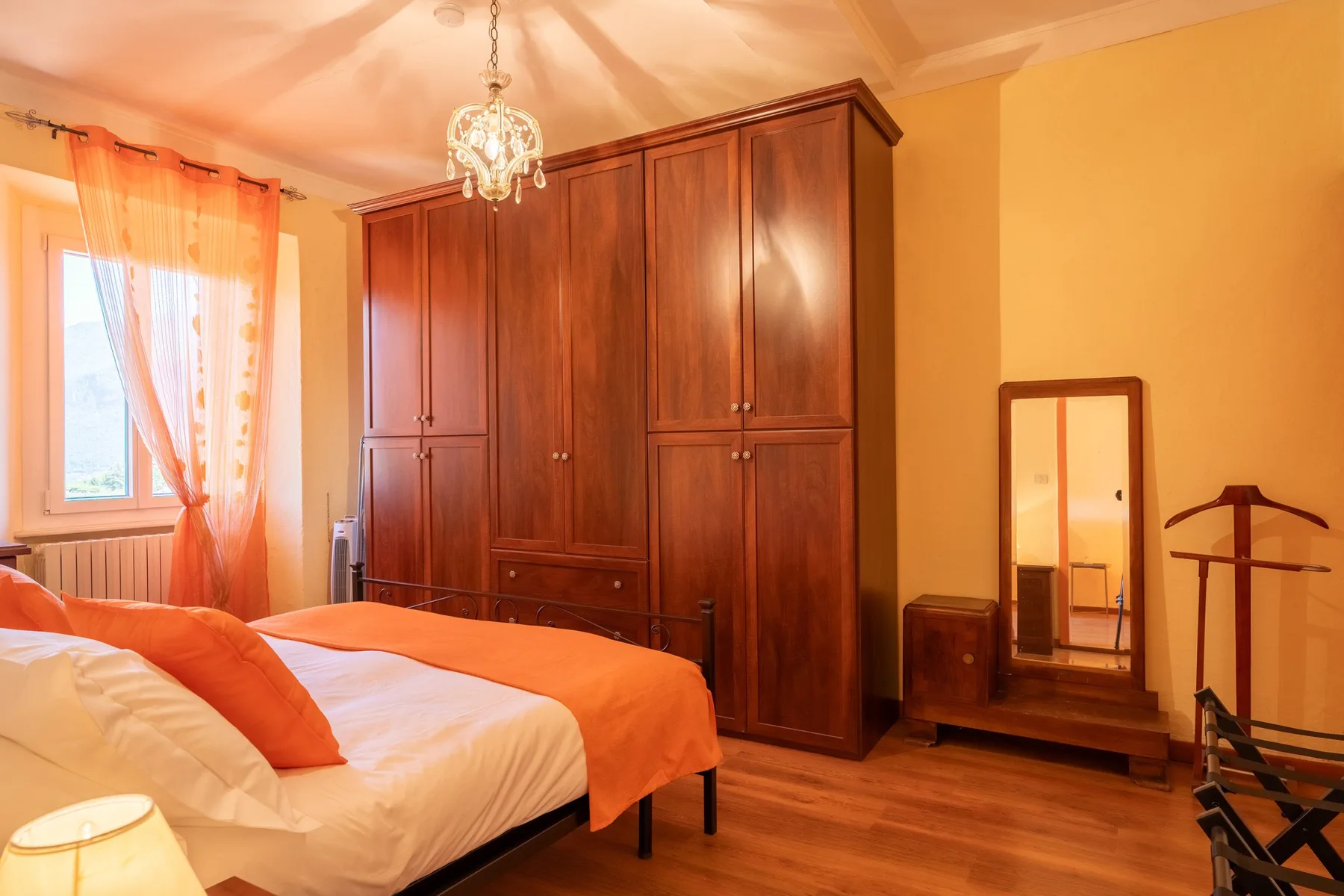 A bedroom with a large wooden wardrobe and a bed dressed in orange and white.