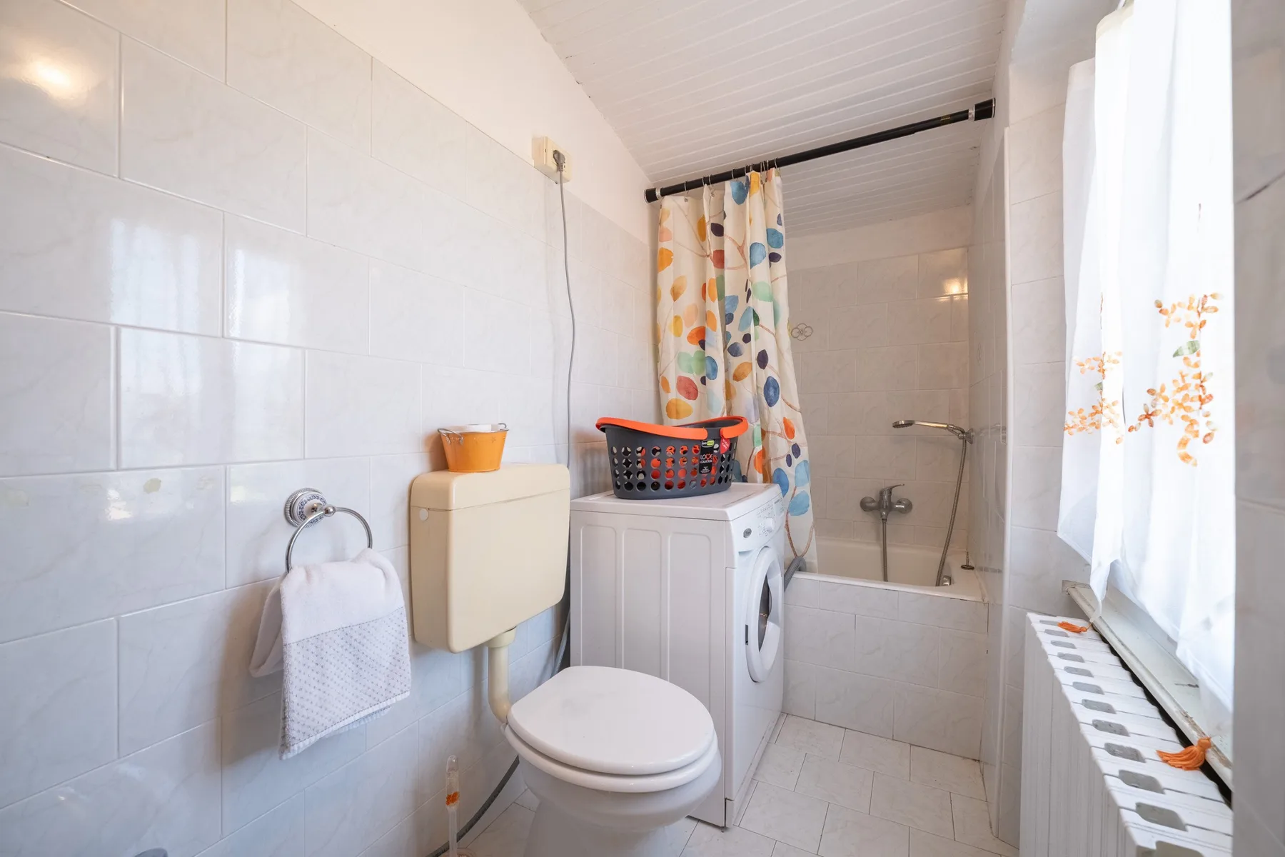 A tiled bathroom with a washing machine, toilet, and shower area.