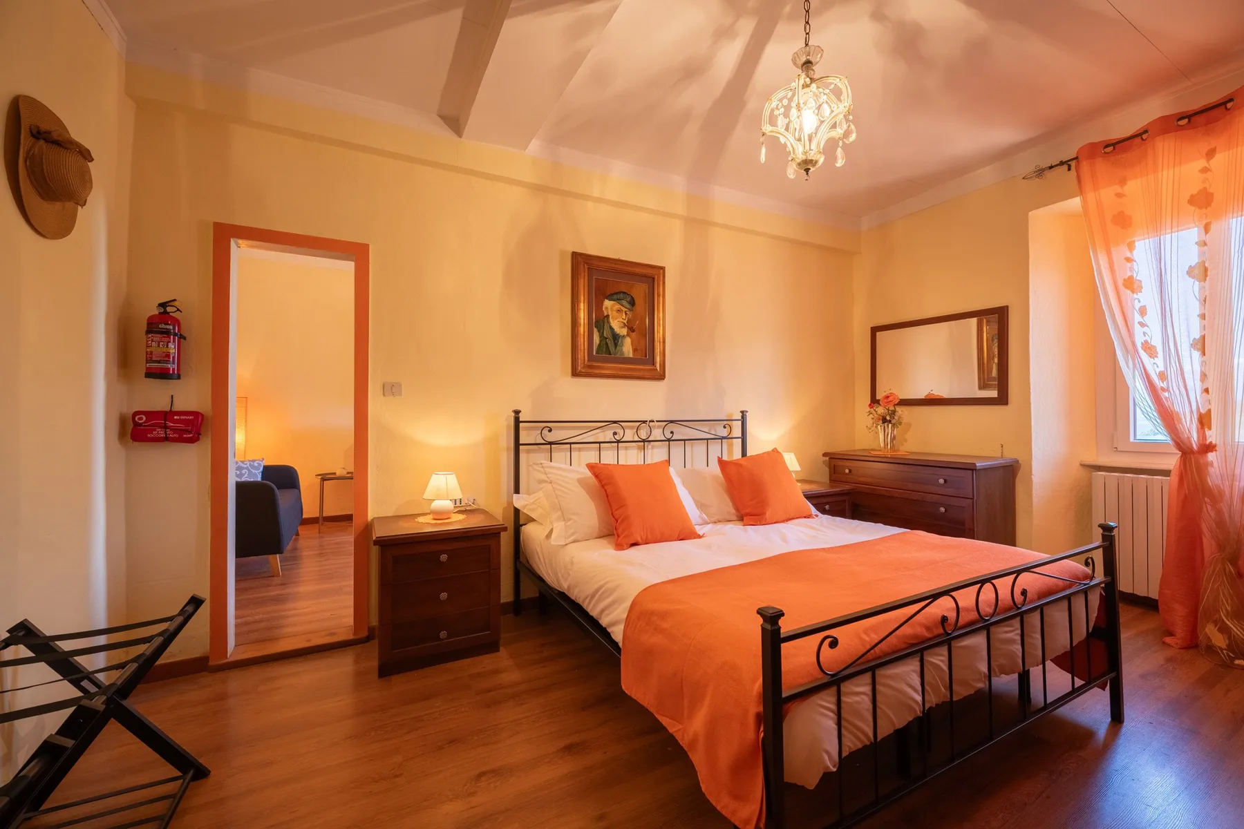 A bedroom with a metal bed, orange bedding, and a wooden bedside table.