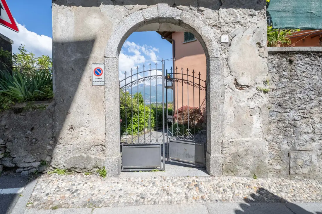 A stone arched entrance frames an iron gate and a view of greenery.