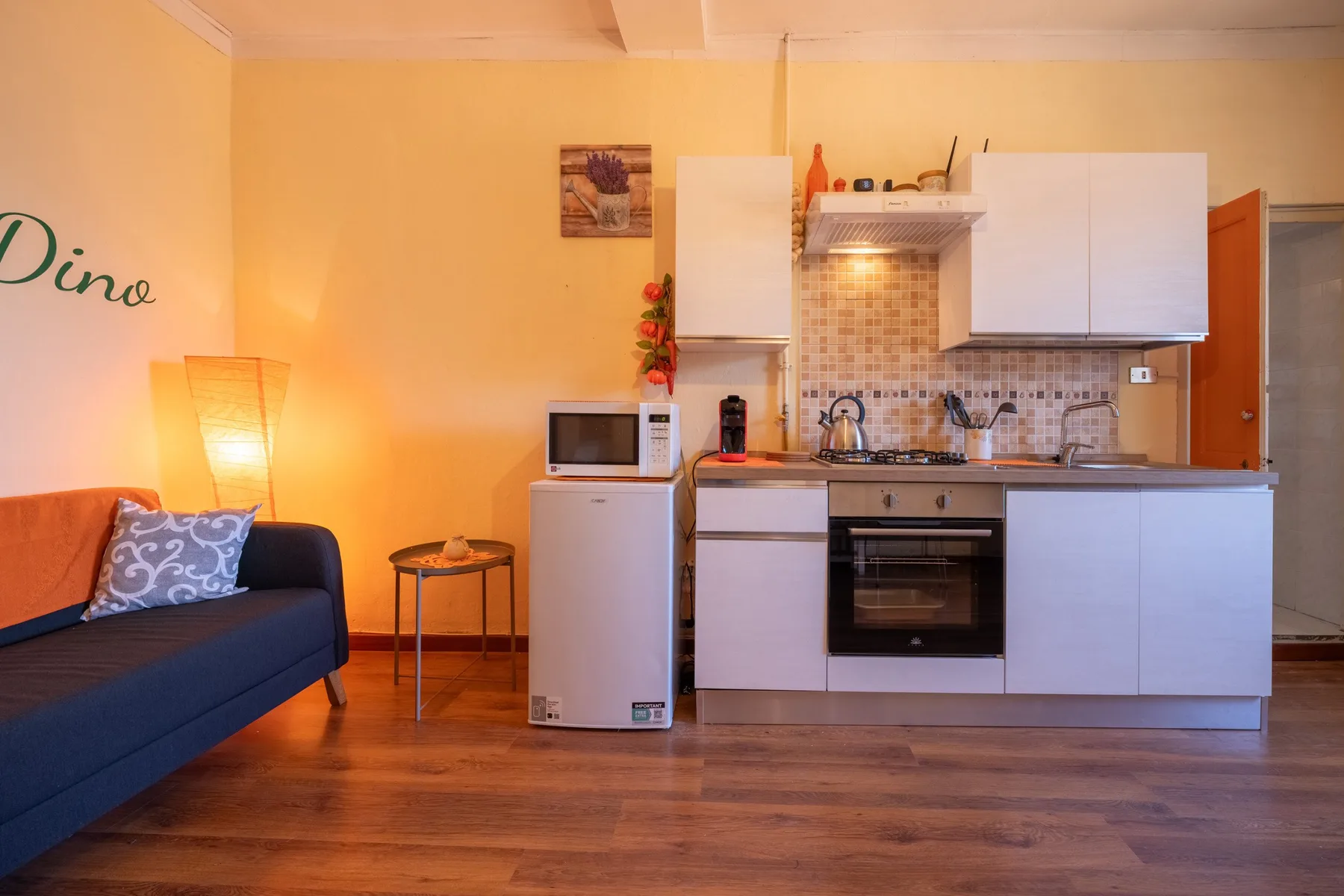 A living area and compact kitchen with a sofa, dining table, and white cabinets.