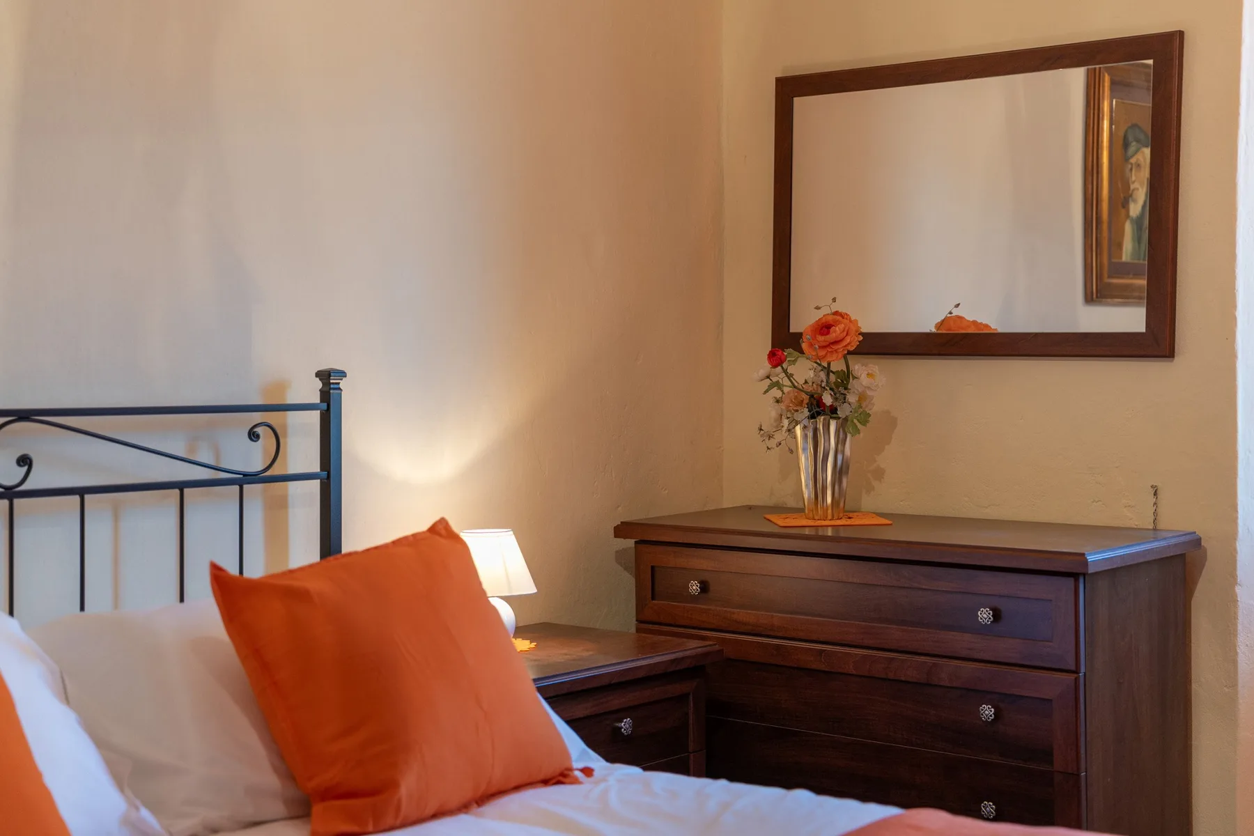 A bedroom with a dark wood dresser, mirror, and orange pillows.