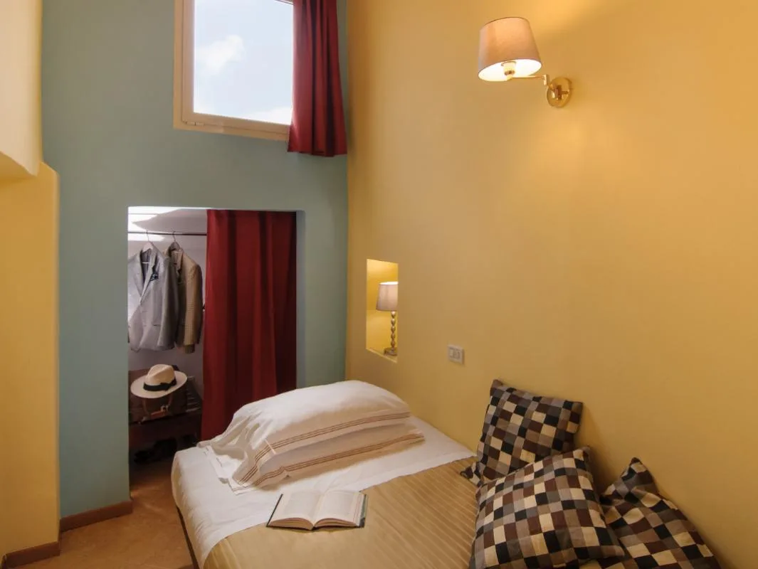 Habitación individual con un armario y una ventana alta.