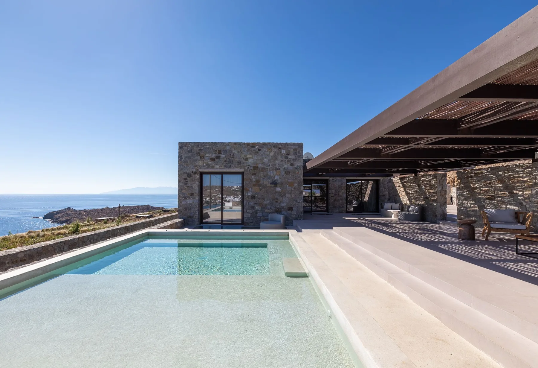 An outdoor pool beside a stone house overlooks the sea.