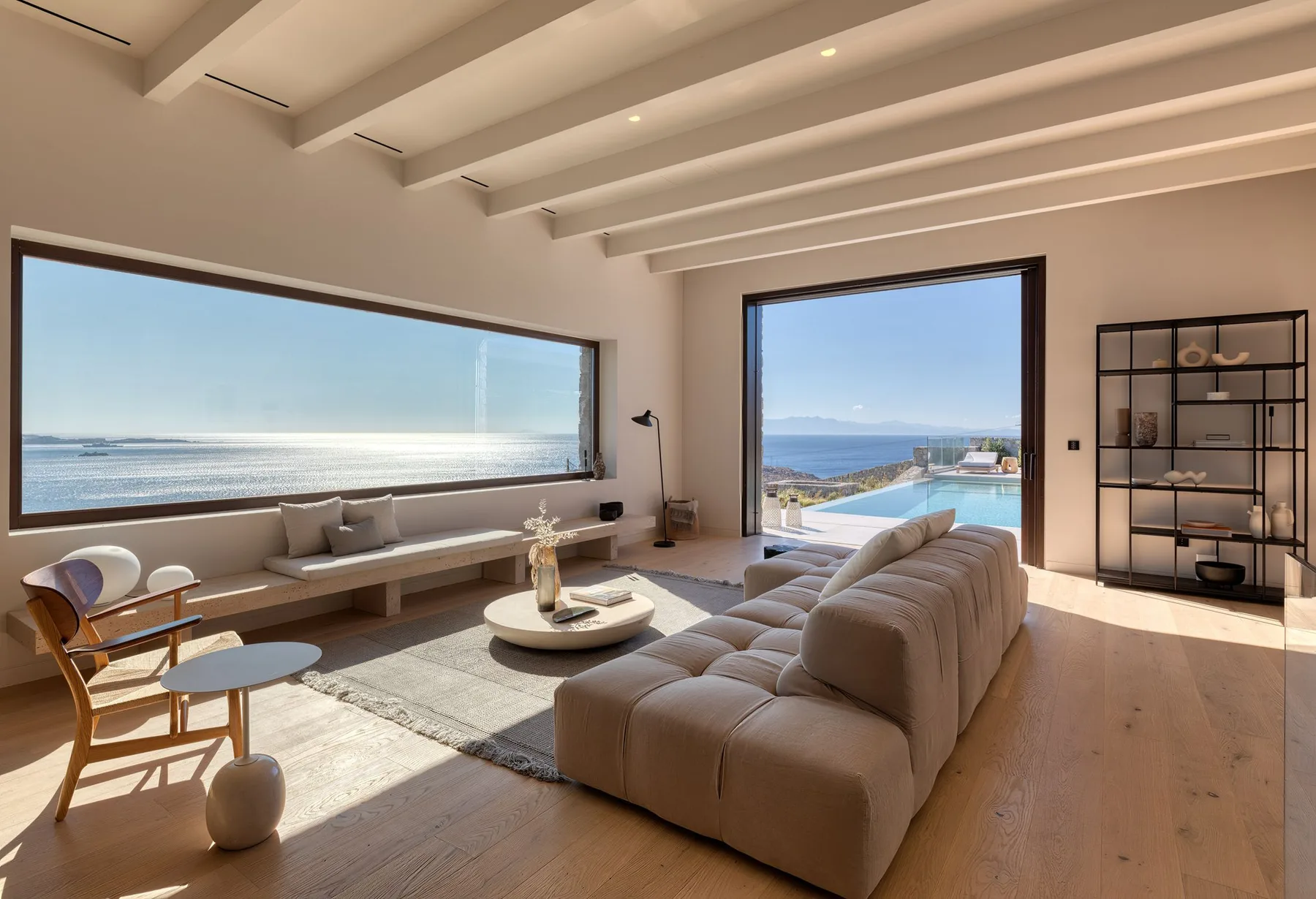 A bright living room with seating, large windows, and a view of the sea.