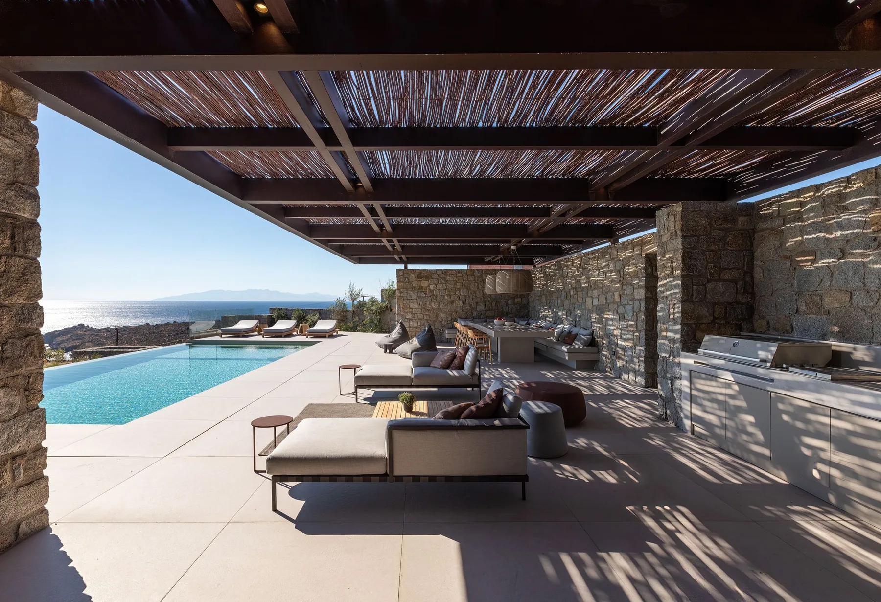 A shaded outdoor lounge beside a pool, with seating and a view of the sea.