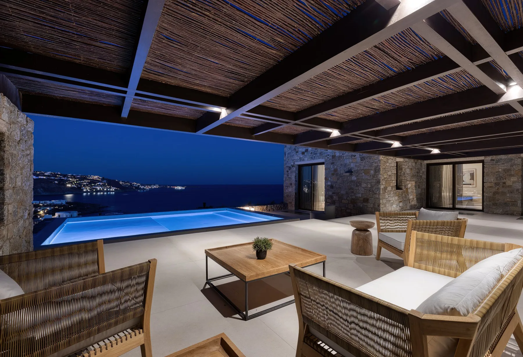 An outdoor pool terrace with seating and a view of the coastline at dusk.