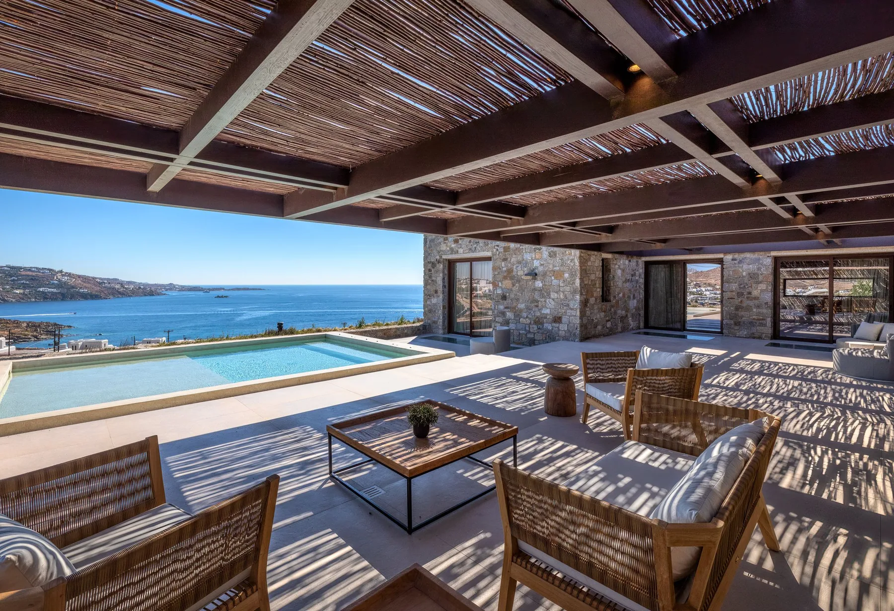 A shaded outdoor terrace overlooks a swimming pool and the sea.