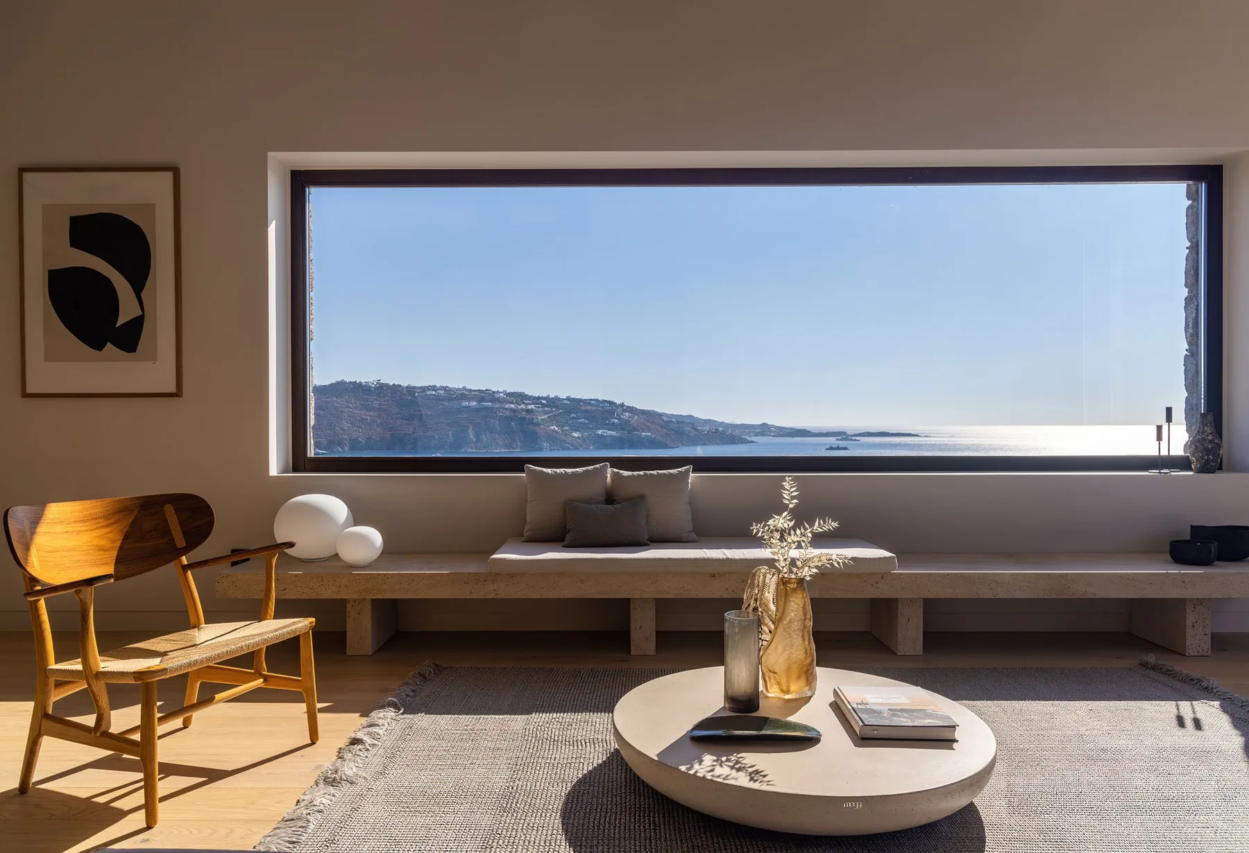 A modern living room with seating facing a wide window overlooking the water.