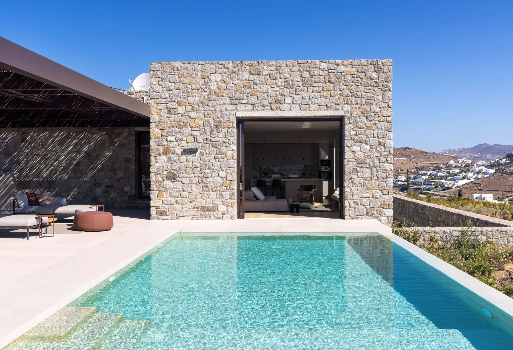 A swimming pool sits beside a stone building with an open doorway.