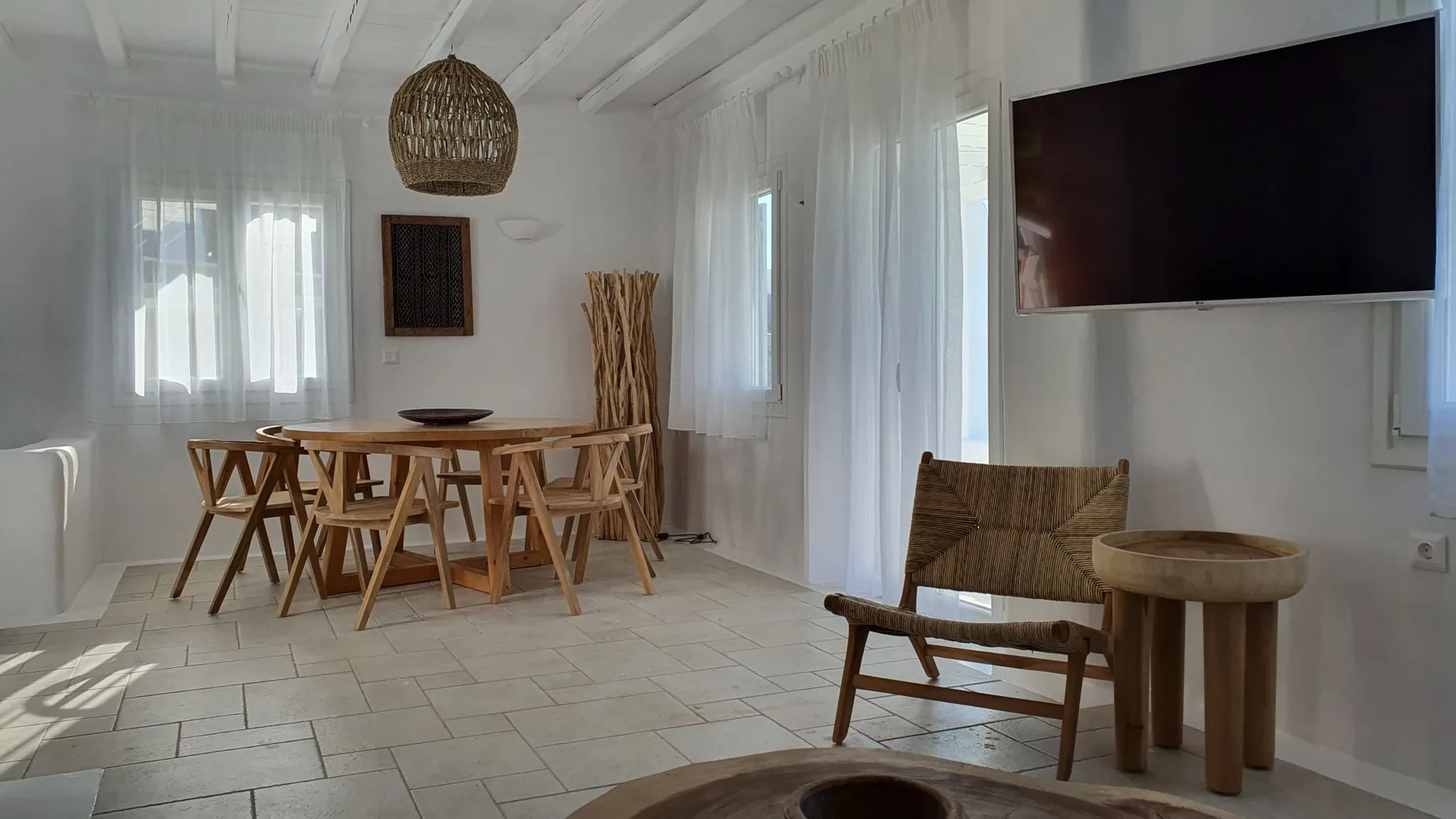 A bright dining area with a wooden table and seating beside a lounge chair.