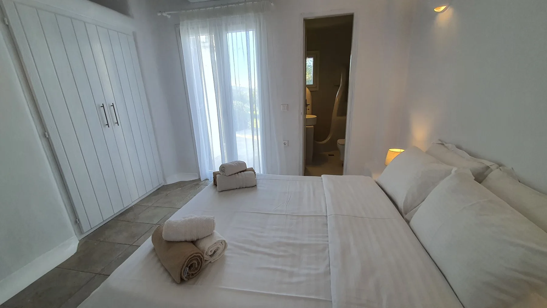 A bedroom with a neatly made bed beside a bright window.