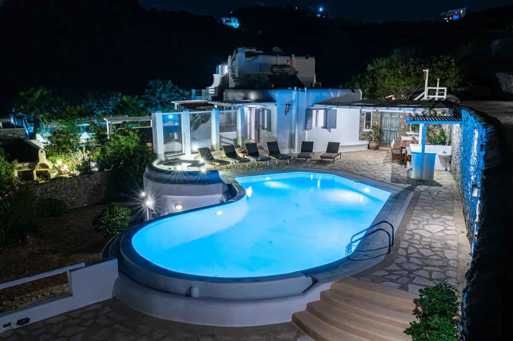 A brightly lit outdoor swimming pool sits beside a modern house at night.