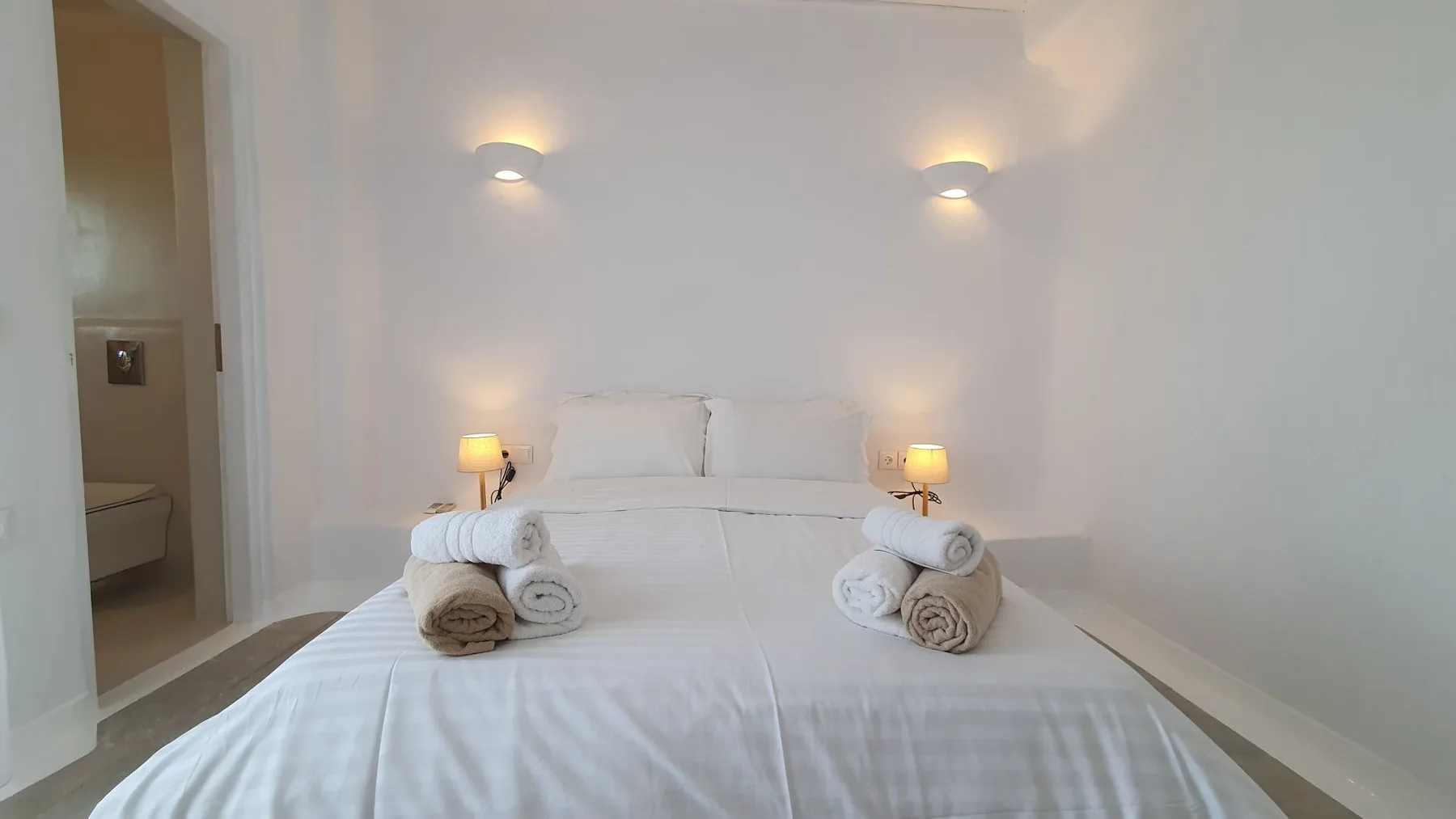 A bright bedroom with a neatly made bed and folded towels.