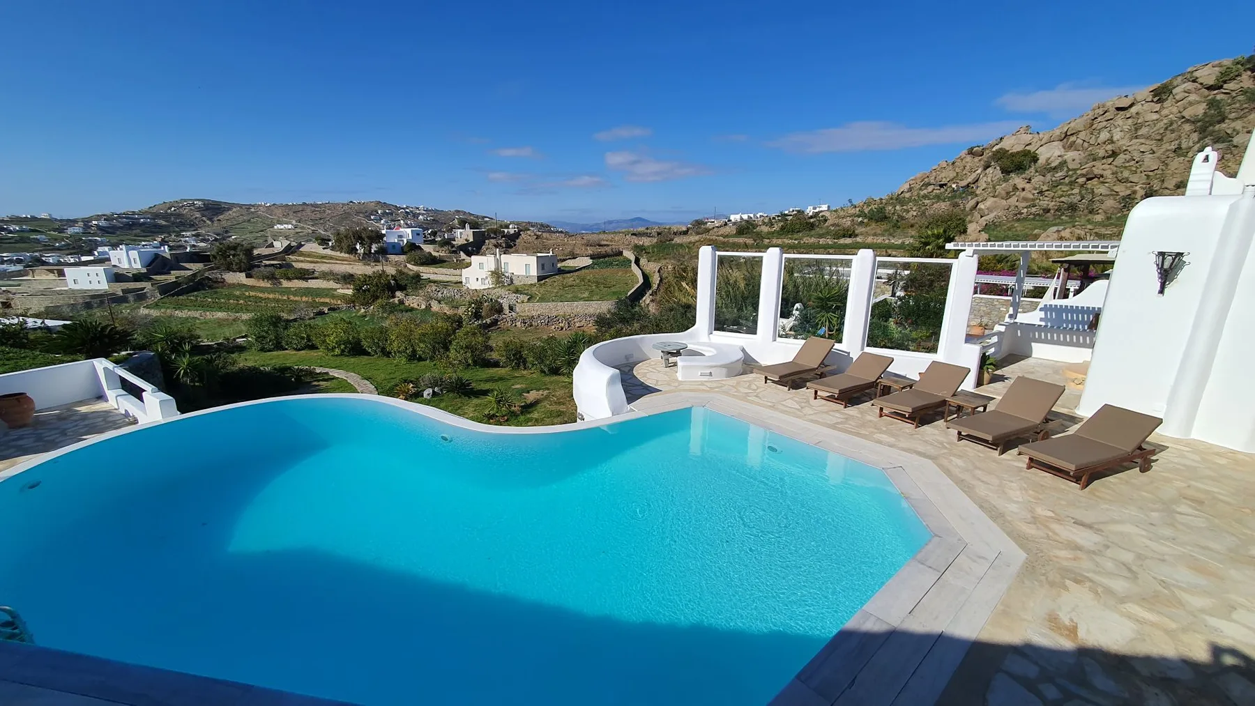 An outdoor swimming pool and sun loungers overlook a hillside landscape.