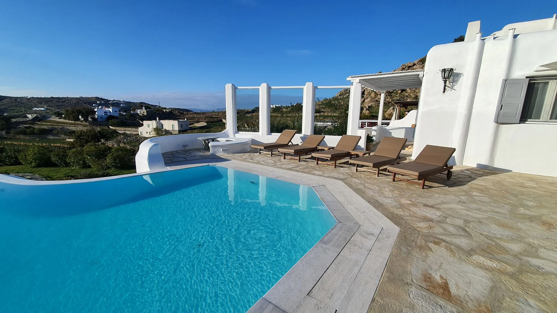 An outdoor swimming pool beside a sunny terrace with loungers.