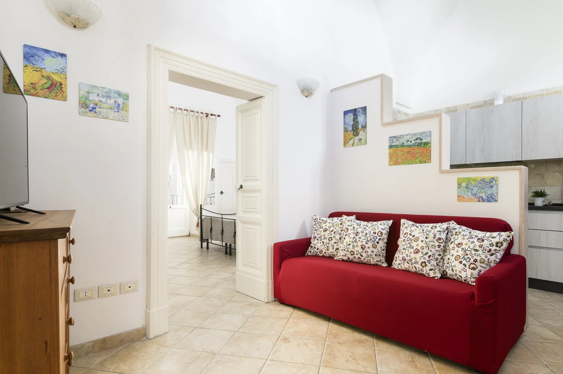 A bright living area with red seating and an open doorway to a dining space.