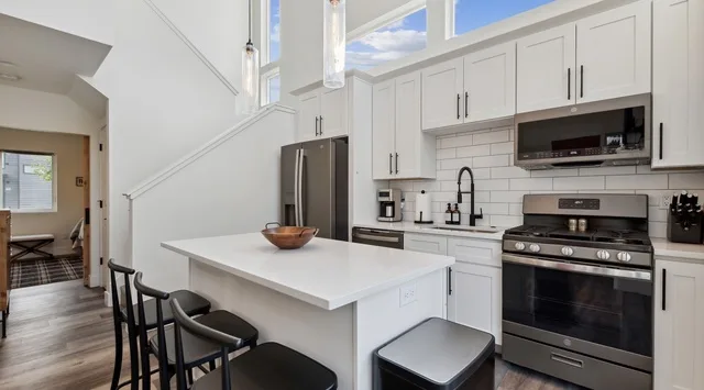 Una cocina luminosa con gabinetes blancos, una isla central y electrodomésticos de acero inoxidable.
