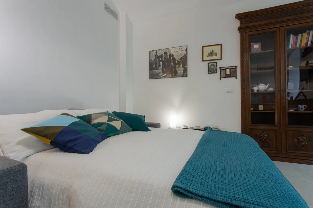 Un dormitorio con una cama bien tendida y almohadas turquesas junto a un armario de madera.