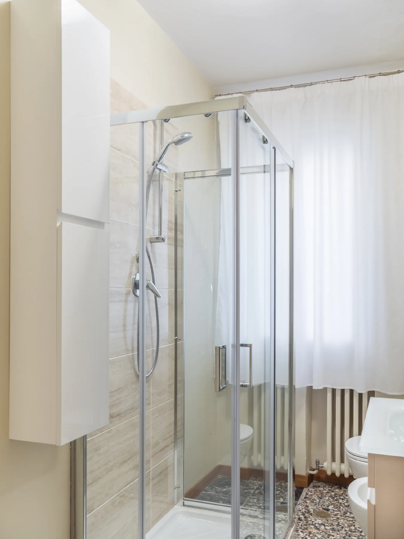 Un baño con ducha de vidrio y un inodoro junto a una ventana con cortina.