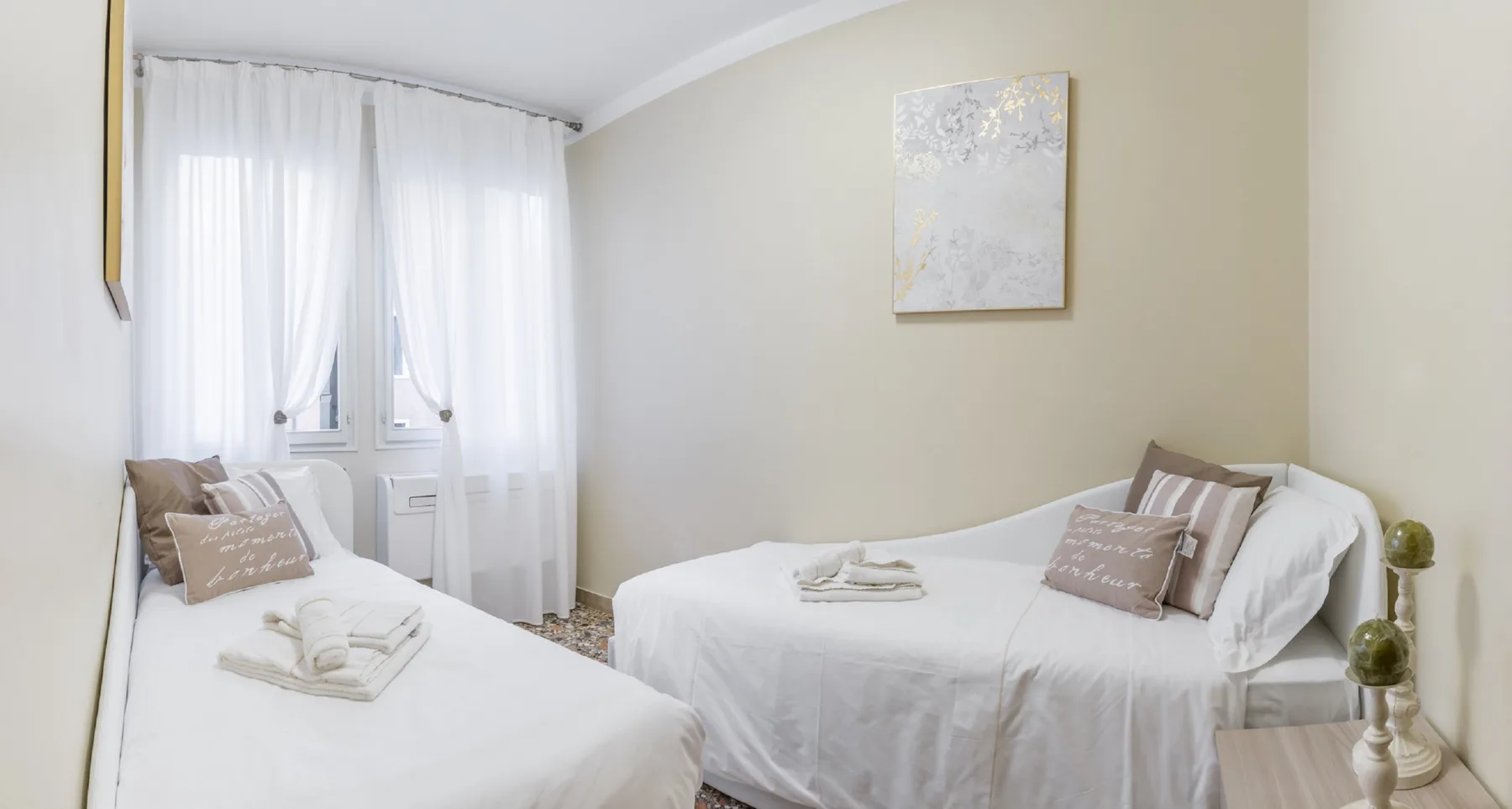 Dormitorio luminoso con dos camas, ropa de cama blanca y cortinas translúcidas.