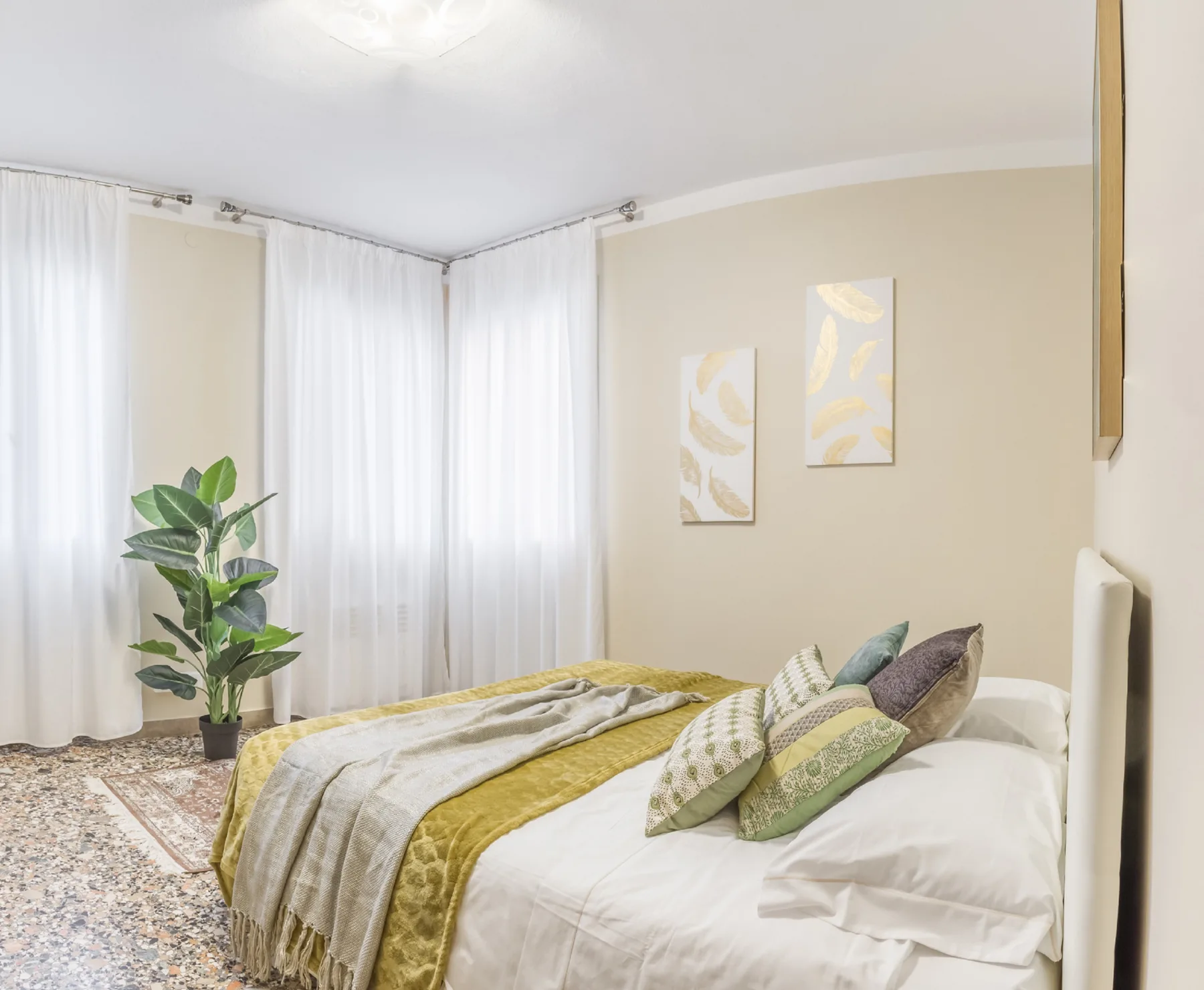 Un dormitorio con una cama, ropa de cama en capas y cortinas translúcidas.