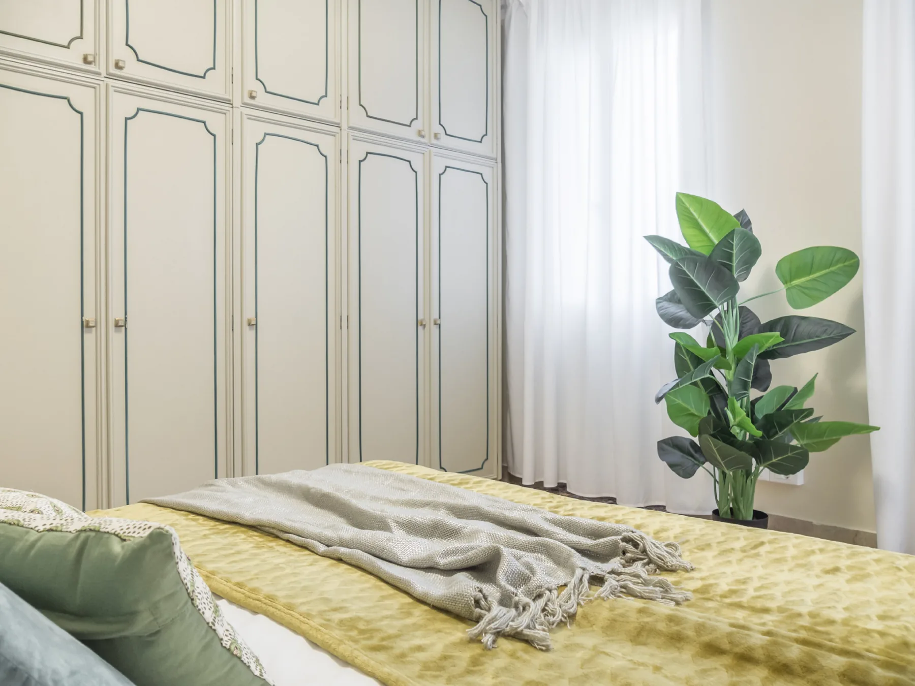 Un dormitorio con una cama cubierta con ropa de cama amarilla y una planta frondosa en maceta.