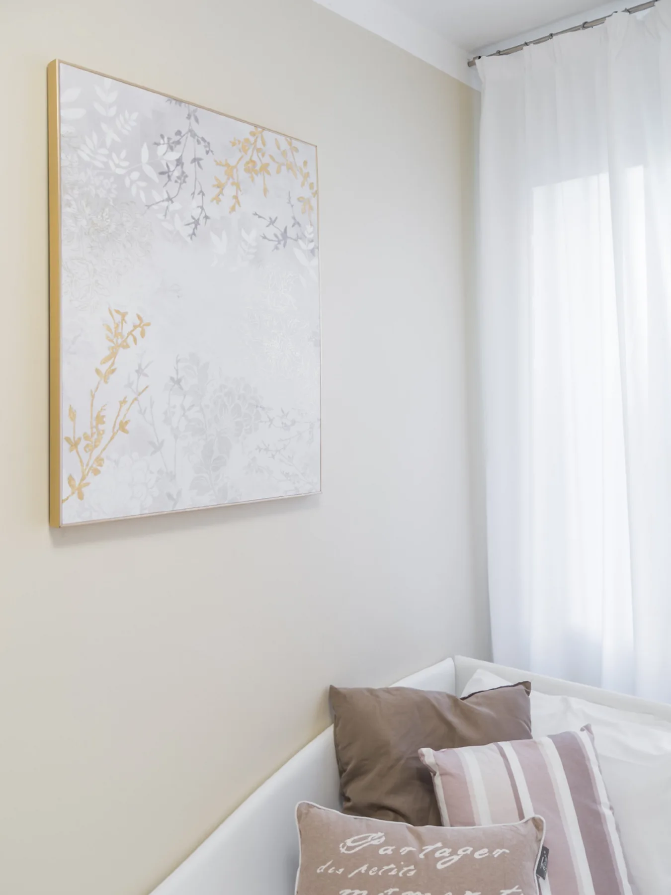 Una esquina de dormitorio con una cama, arte decorativo en la pared y cortinas translúcidas.