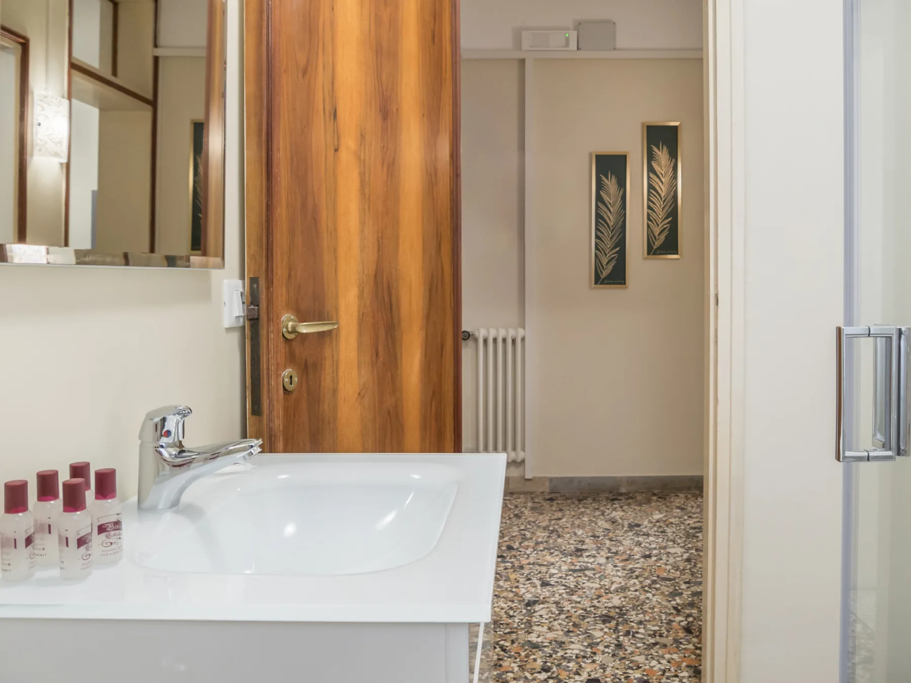 Un lavabo de baño da a un pasillo con suelo estampado y arte botánico enmarcado.