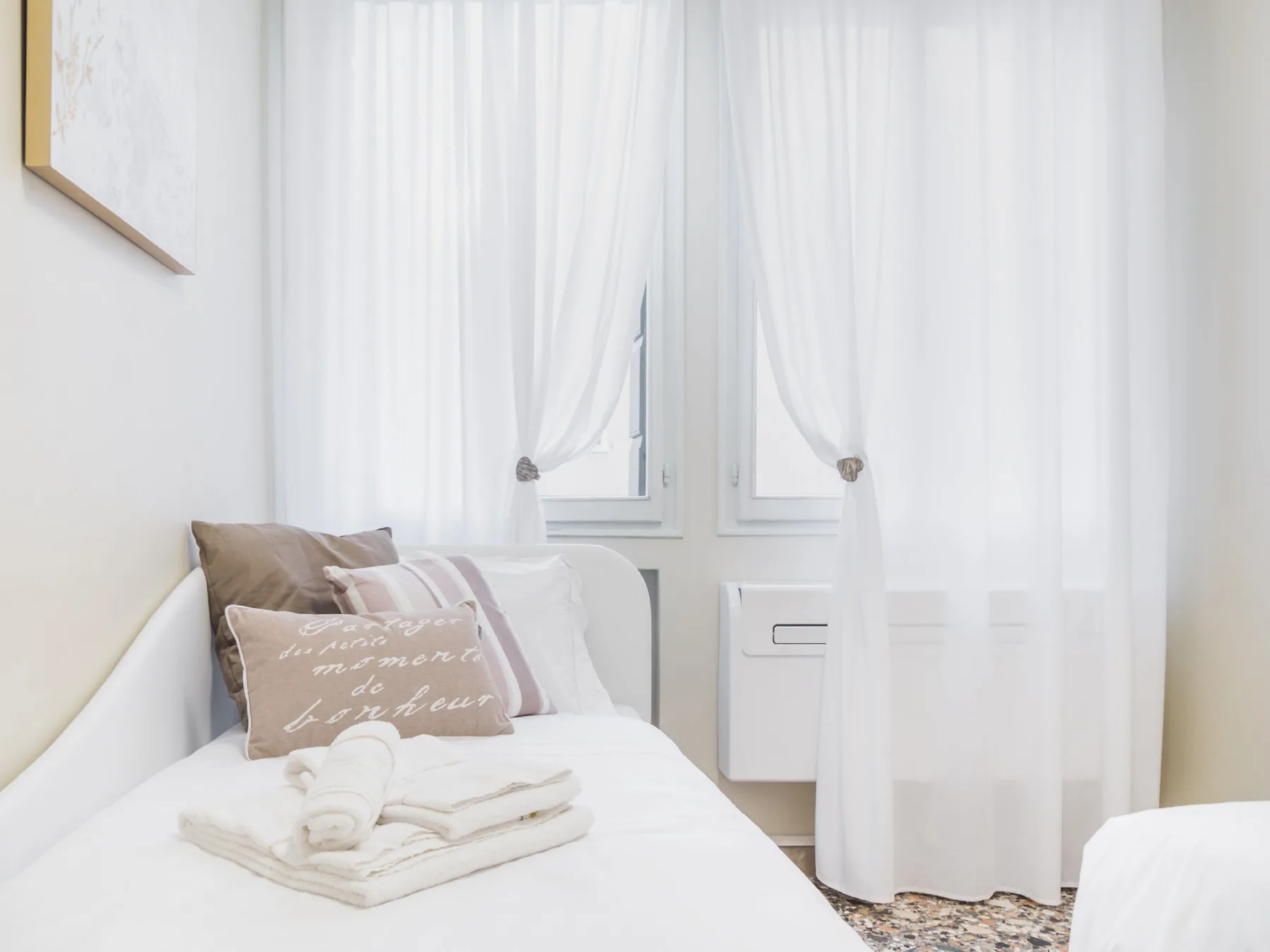 Un dormitorio luminoso con una cama bien hecha y cortinas translúcidas en la ventana.