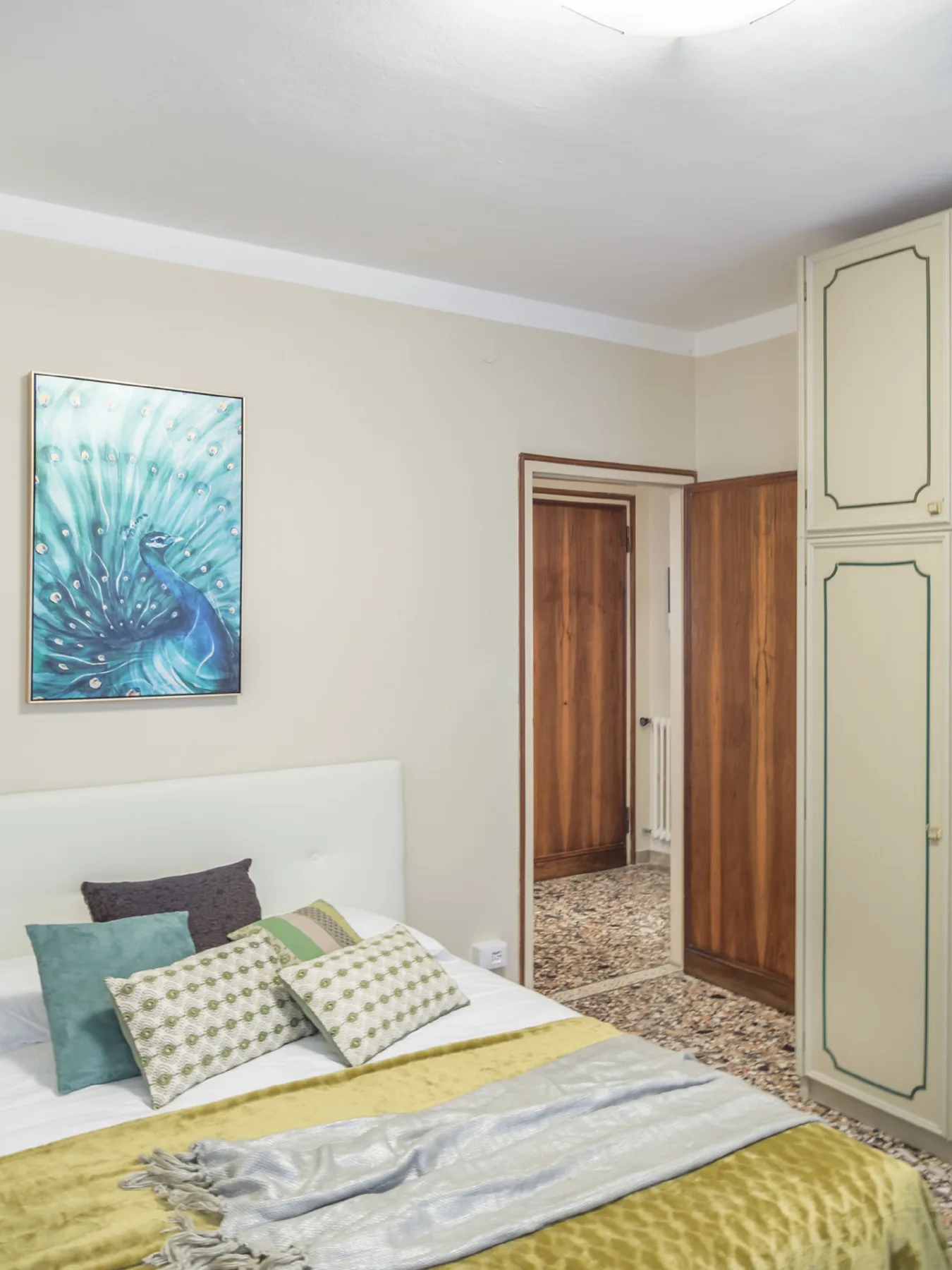 Dormitorio con una cama, cojines estampados y una pintura de un pavo real en la pared.