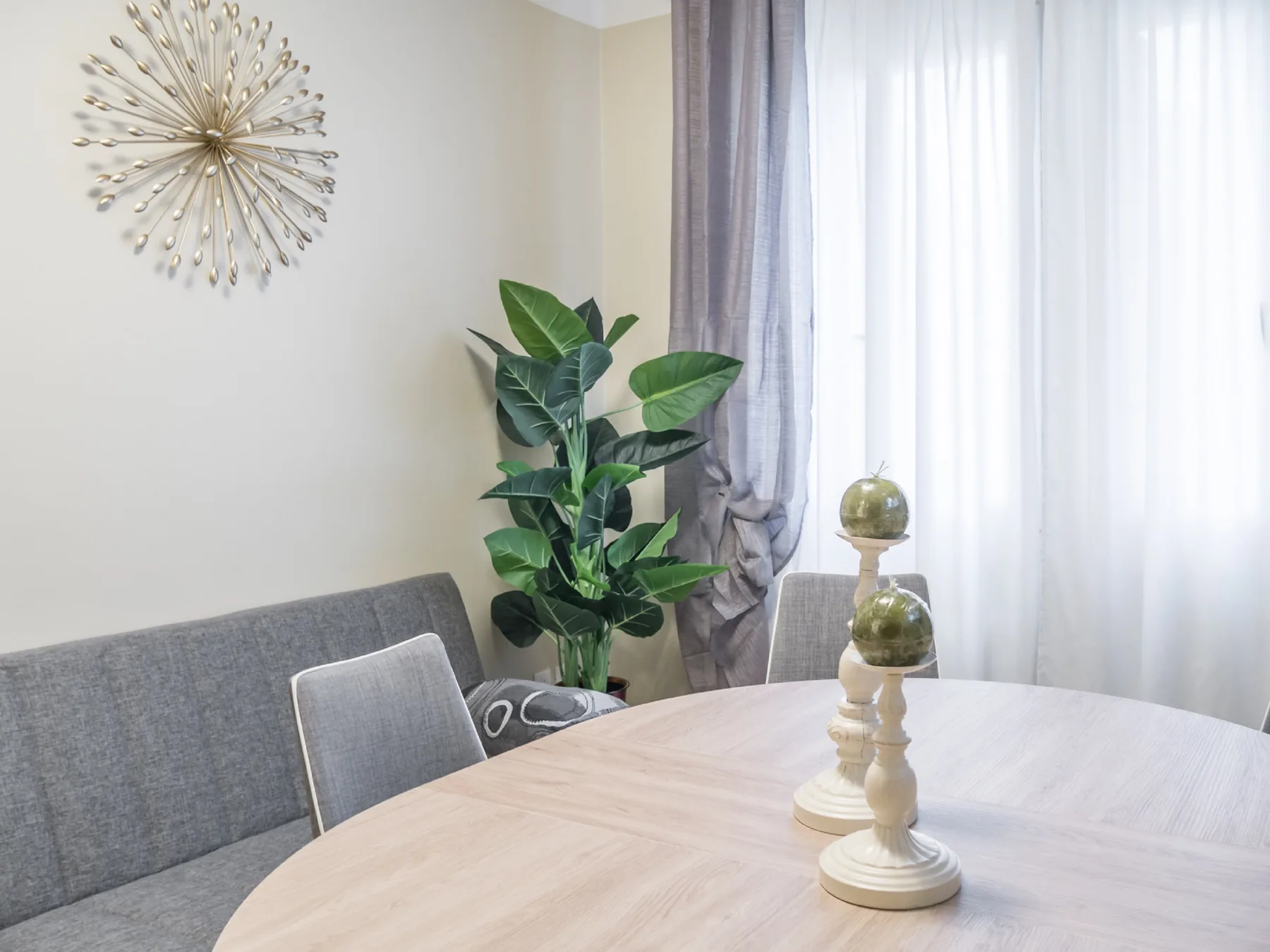 Un comedor con una mesa de madera clara, asientos tapizados y una planta frondosa.