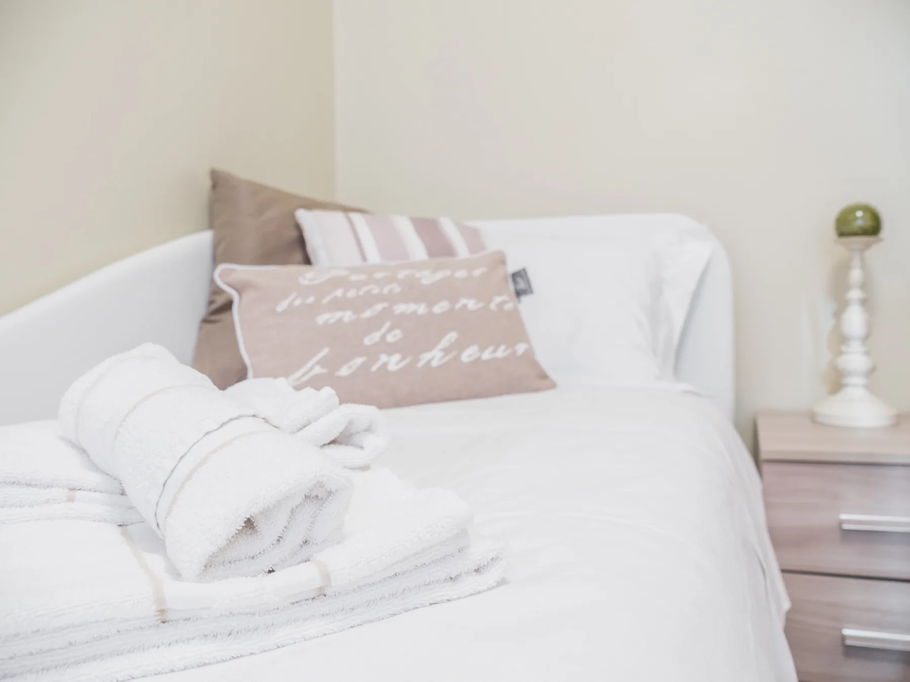 Una cama bien tendida con toallas blancas dobladas y cojines decorativos.
