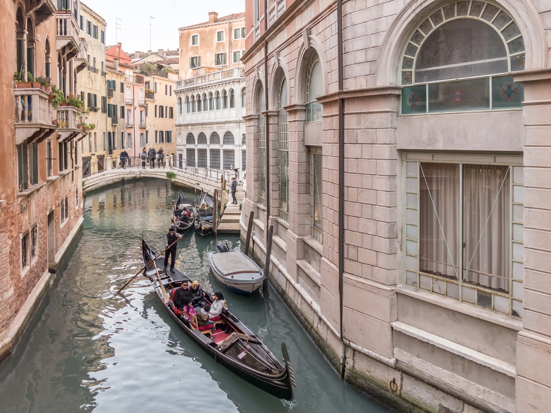Un canal estrecho pasa entre edificios históricos mientras góndolas navegan bajo un pequeño puente.