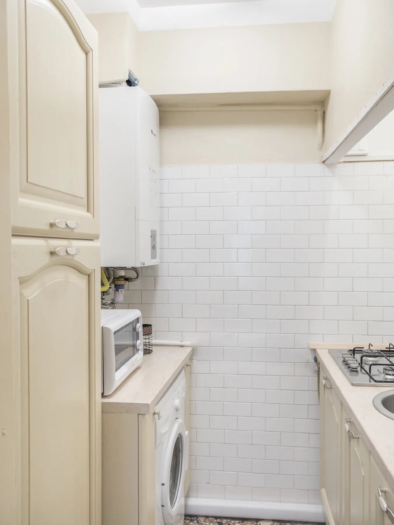 Una cocina pequeña con paredes de azulejos, un microondas y una lavadora.