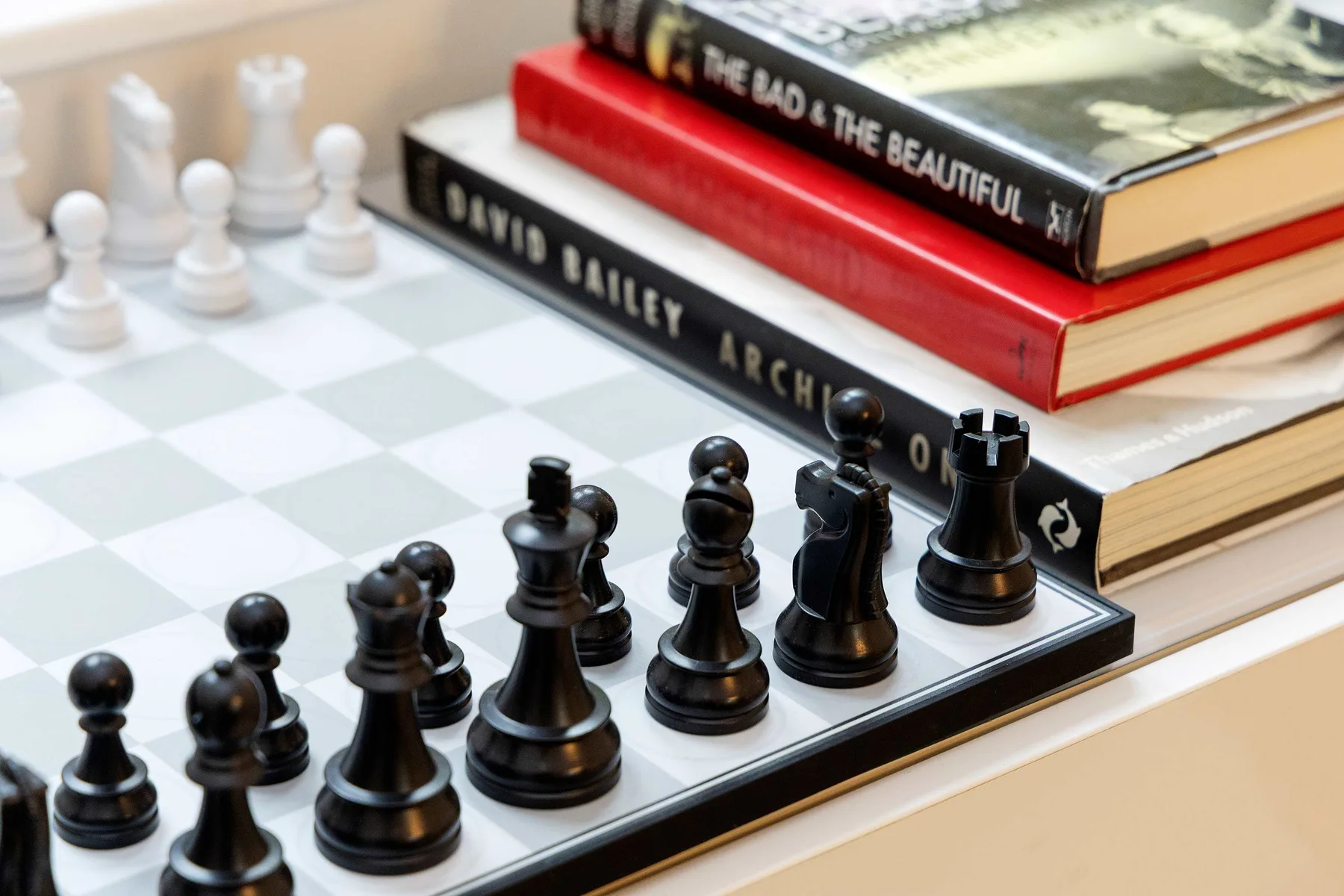 A chessboard with black pieces sits beside a stack of books.