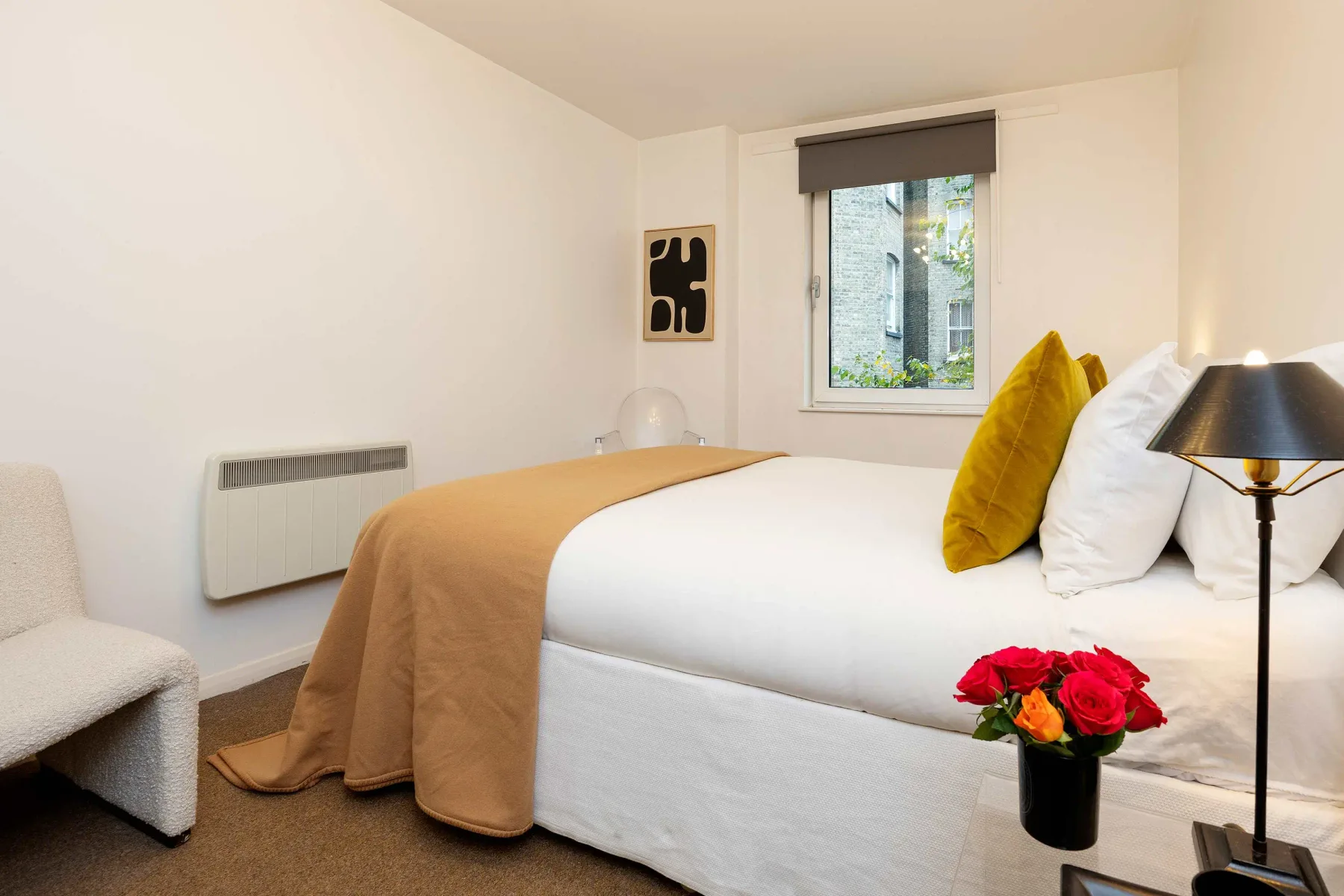 A bedroom with a neatly made bed and a window overlooking greenery.
