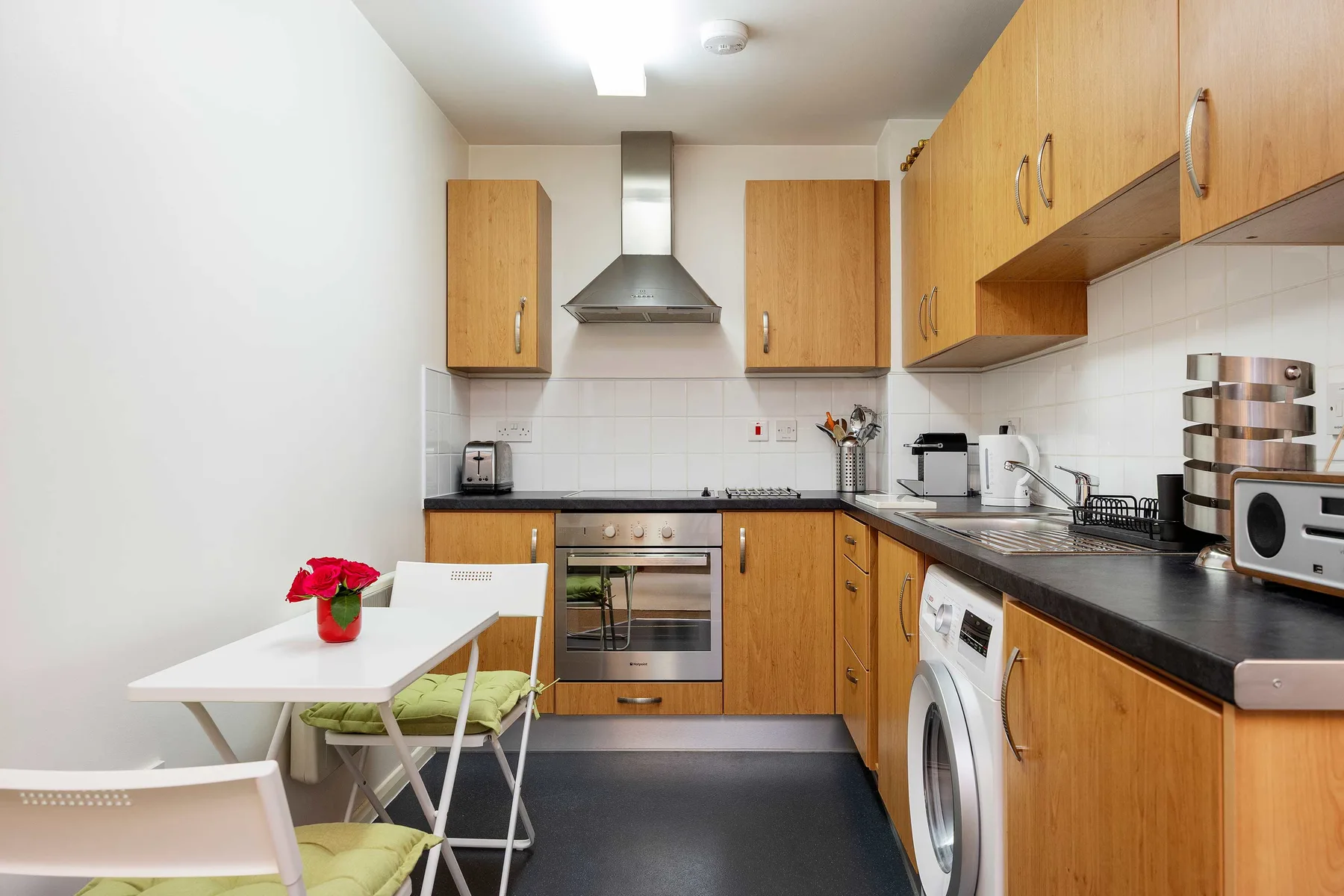 A compact kitchen with wooden cabinets, dark counters, and a small dining table.