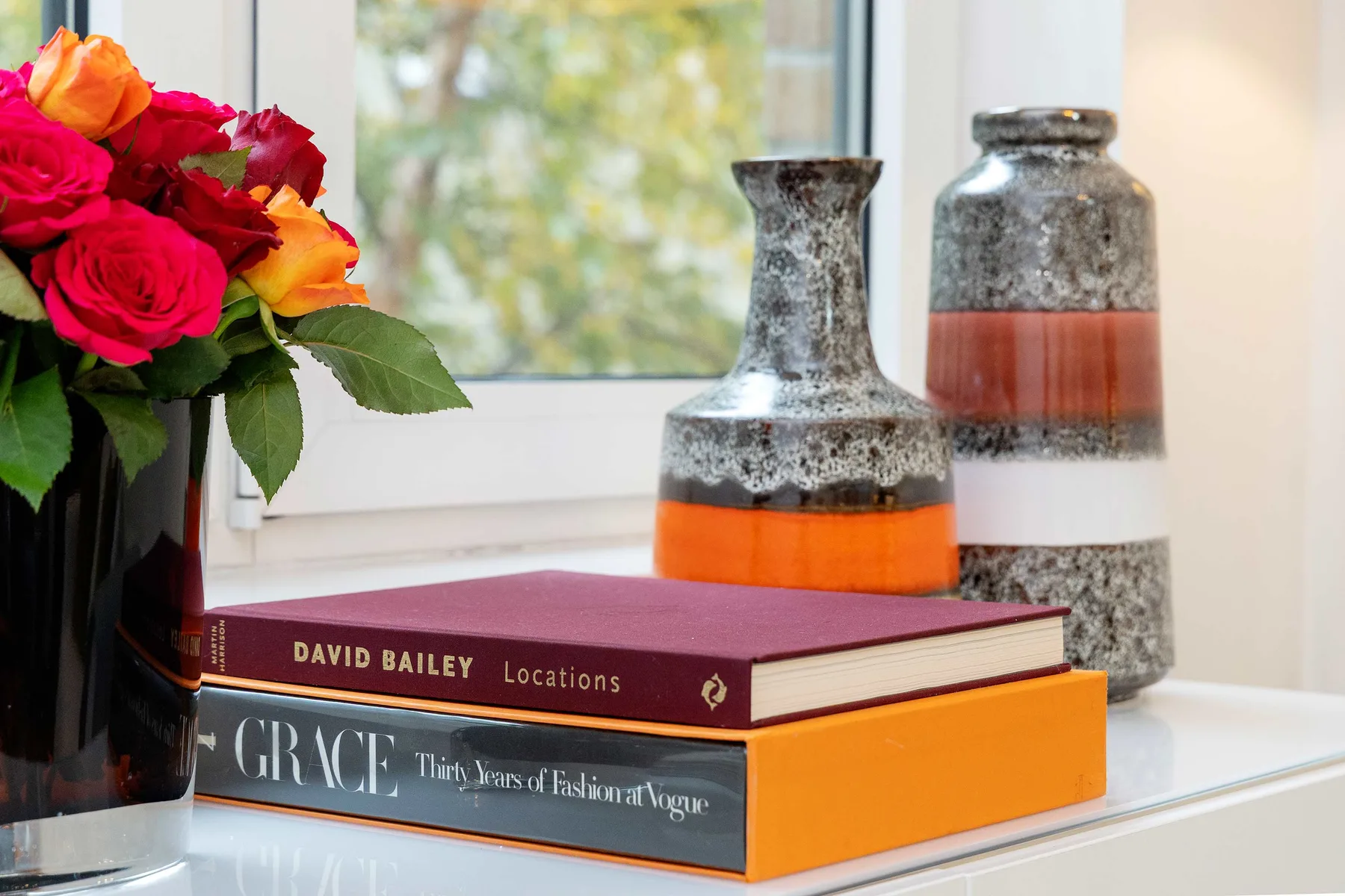 A still life of colorful flowers and decorative vases beside stacked books on a table.