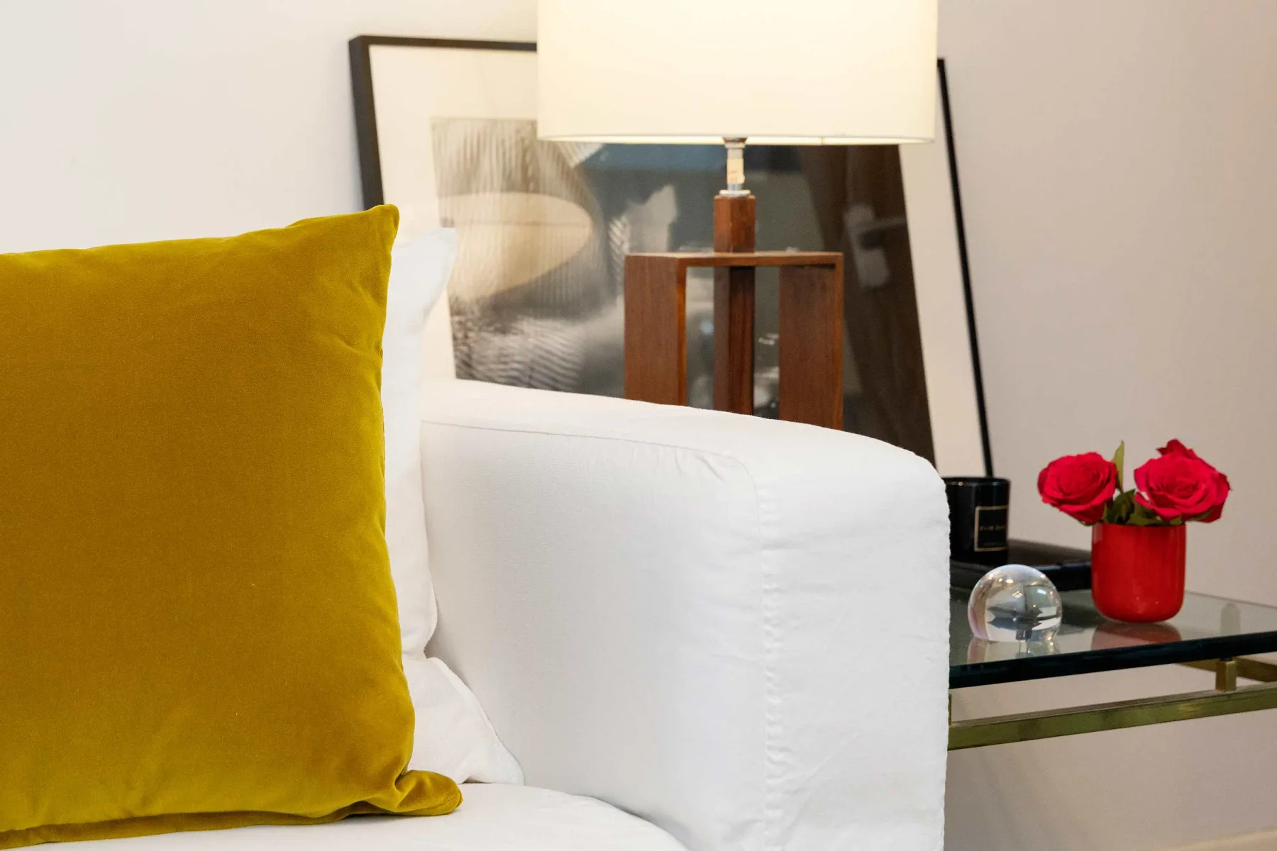 A bedroom seating area with a white sofa, mustard cushion, and table lamp.