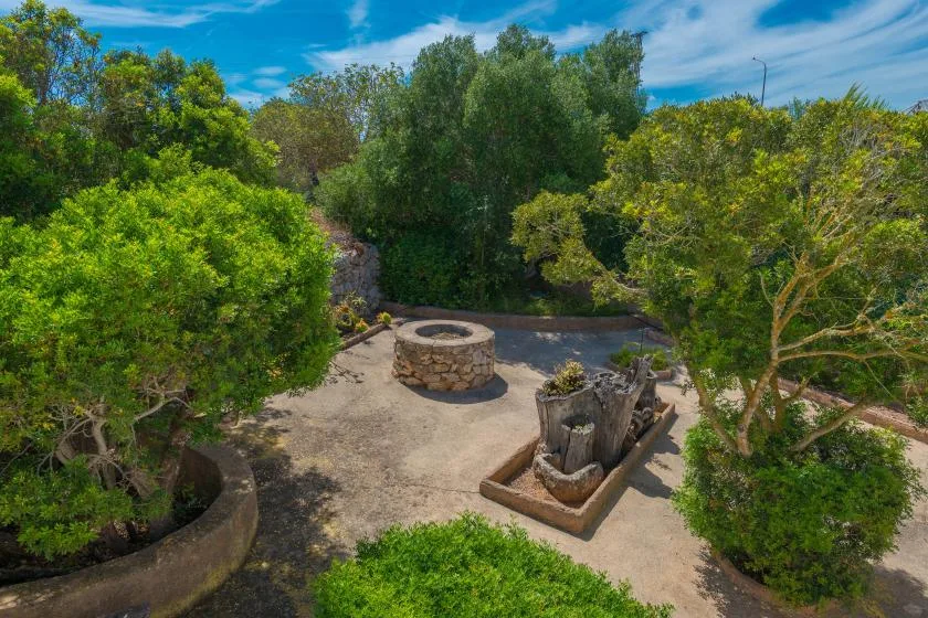 Un pozo de piedra y una jardinera están en un jardín rodeado de árboles.
