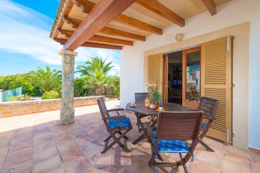 Un patio sombreado con asientos al aire libre y contraventanas de madera da a un jardín.