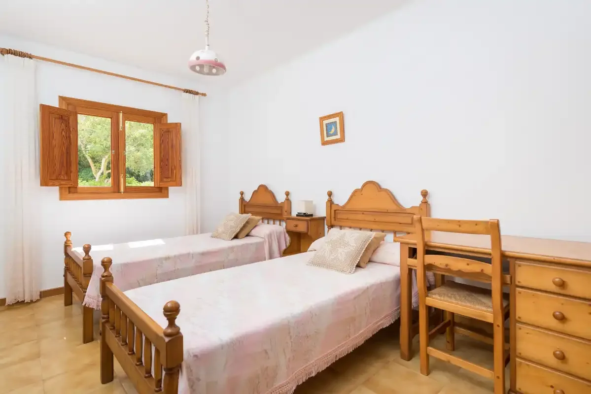 Dormitorio con camas de madera, un escritorio y una ventana con vistas a la vegetación.
