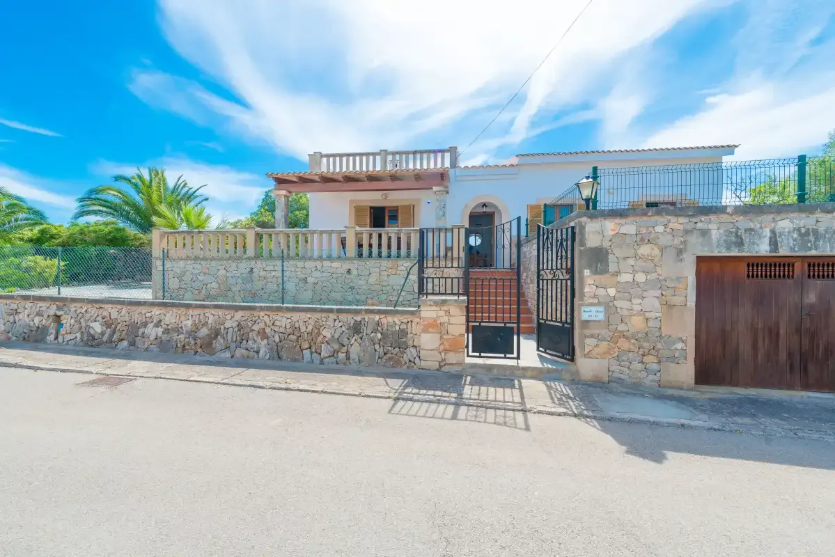 Entrada de una propiedad con muro de piedra, puerta metálica y acceso para vehículos.