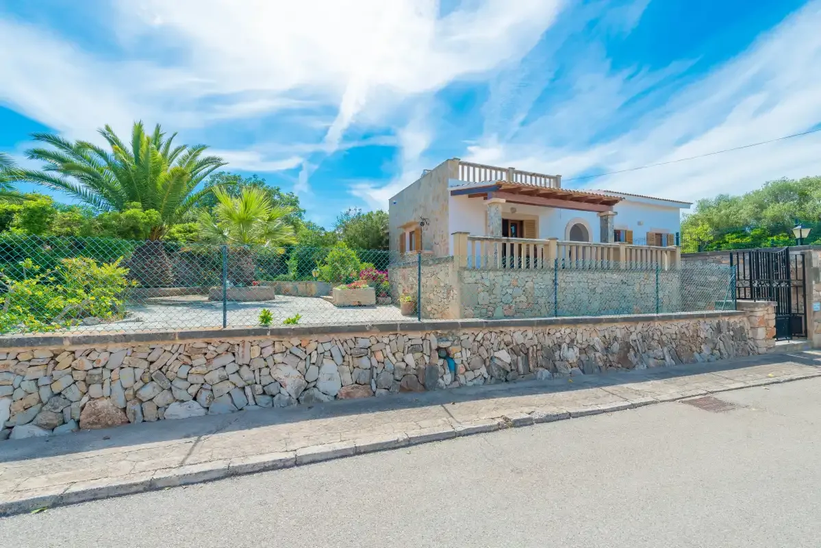 Una casa baja con un muro de piedra y palmeras en el patio.