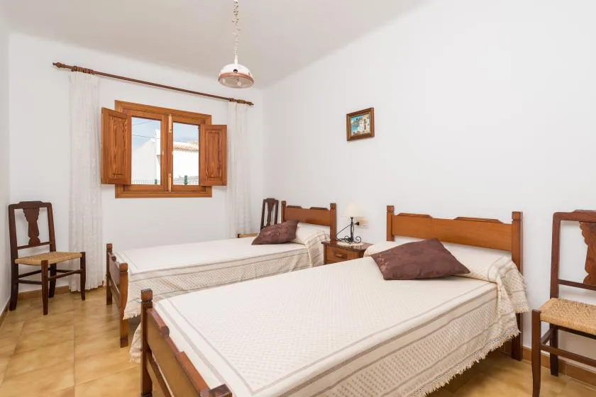 Un dormitorio con dos camas, contraventanas de madera y sillas.