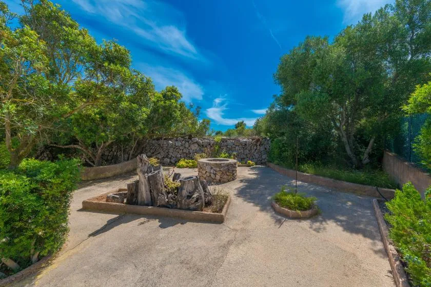 Un patio exterior pavimentado con un muro de piedra y árboles frondosos.