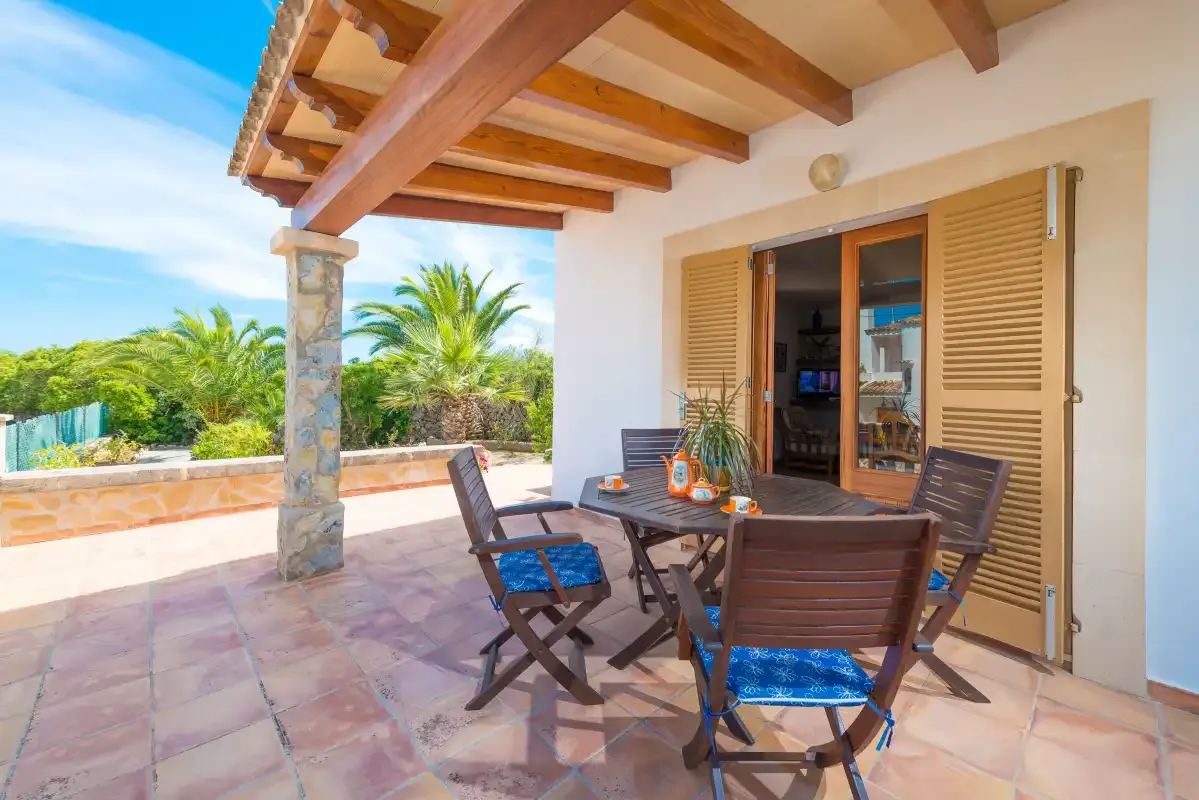 Un patio cubierto tiene una mesa de comedor y asientos junto a las puertas abiertas.