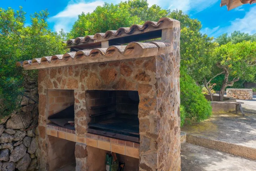 A stone outdoor fireplace stands beside trees and a paved patio.