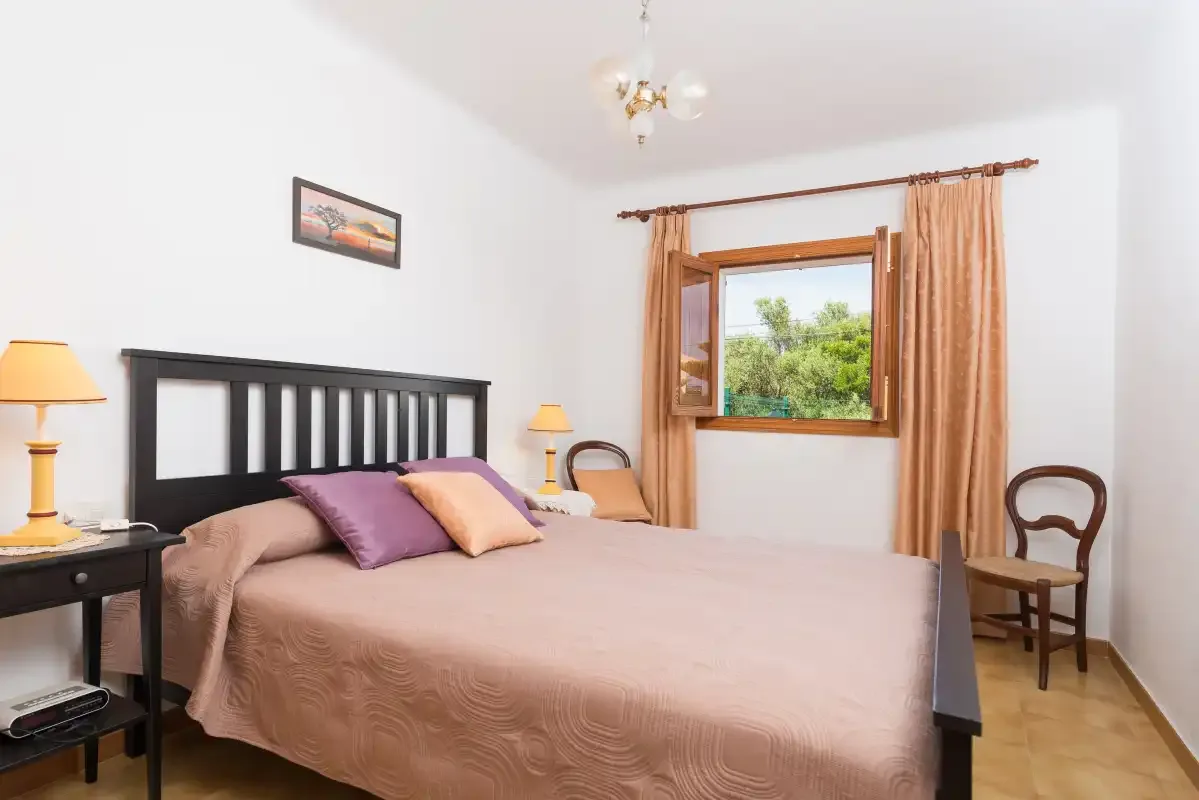 Dormitorio con una cama grande, lámparas de noche y una ventana con vistas a la vegetación.